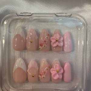 Press-on naglar med 3D-blommor och pärlor - Säljer ett set med press-on naglar i ljusrosa och nude toner. Naglarna har dekorativa 3D-blommor, små pärlor och guldiga detaljer. Några naglar har vit fransk tipp och andra är dekorerade med små blommor och pärlor för en söt och trendig look. Ingår då också nagelvårdssätt