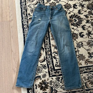 Levis 501 blå jeans - Klassiska blå Levis 501 jeans med raka ben och normal passform. Som har storleken 158/162. Jeansen har slitna detaljer framtill och femficksdesign. De är tillverkade i robust denim och har knappgylf samt Levis-logga på bakfickan.