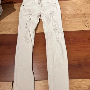 Vita ripped jeans från Sneak Peek - Säljer ett par vita jeans från Sneak Peek med flera slitningar framtill. Byxorna har fem fickor, normal passform och raka ben. Perfekta för en trendig och avslappnad look.