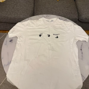 Vit t-shirt 0ff-White - Vit t-shirt från 0ff-White med svart tryck på bröstet. Klassisk rund halsringning och korta ärmar. Perfekt för en stilren och trendig look. Bra skick. Skickar alltid inom 24 timmar.