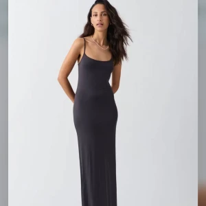 Svart långklänning med smala axelband - En stilren mörkgrå långklänning med smala axelband och figurnära passform. Klänningen har en enkel och elegant design med rundad urringning och rak siluett. Perfekt för dig som gillar minimalistisk stil. Klänningen är från Gina tricot och är knappt använd 