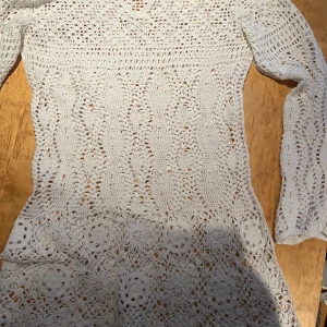 Vit virkad klänning från Paon - Superfin vit virkad klänning från Paon med lång ärm och v-ringning. Klänningen har ett detaljerat spetsmönster och är figurnära i modellen. Perfekt för sommarens alla tillfällen!