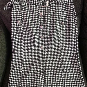 Svartvit houndstooth klänning från River Island - Säljer en snygg svartvit klänning från River Island med klassiskt hundtandsmönster. Klänningen har knappar framtill och en markerad midja. Perfekt för dig som gillar tidlös stil med en twist. Endast provat en gång vilket passar den inte alls för min storlek, dvs fel storlek för mig. 