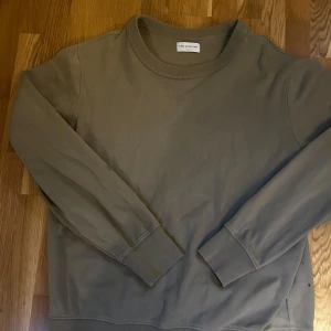 These Glory Days Sweatshirt - Säljer en stilren Oliv färgad sweatshirt från These Glory Days i storlek medium. Tröjan har rund halsringning, långa ärmar och ribbade muddar vid ärmslut och nederkant. Perfekt för en avslappnad och snygg look.