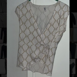 Vit omlottblus med mönster från Chiara Forthi - Säljer en vit omlottblus från Chiara Forthi med guldigt grafiskt mönster. Blusen har knyt i sidan, v-ringning och är ärmlös. Materialet är glansigt och känns lyxigt.