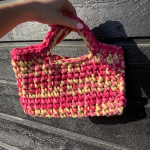 Handgjord virkad väska i rosa och gul - Säljer en unik handgjord väska med breda band. Väskan har ett mjukt och chunky utseende. Perfekt för dig som vill sticka ut med en färgglad accessoar.