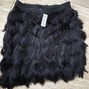 Svart mini kjol med pälsfrill oanvänd  - Säljer en svart kjol med långa, fluffiga pälsdetaljer som ger en cool och unik look. Kjolen har resår i midjan och är perfekt för dig som vill sticka ut. Passar till många olika stilar och är ett riktigt statement-plagg. Passar s-m 