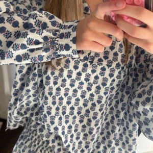 Vit och blå blommigt sätt - Supersöta sättet med vitt tyg och blått blommönster. Sättet har långa ärmar med resår vid handlederna och en smockad midja som ger en fin passform. Perfekt för vår och sommar!