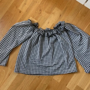 Svartvit rutig offshoulder-blus från NLY Trend - Säljer en svartvit rutig blus från NLY Trend med offshoulder-modell och långa ärmar. Blusen har volangdetalj upptill och är perfekt för dig som gillar en trendig och avslappnad stil. Ganska stor i storleken så sitter som en M