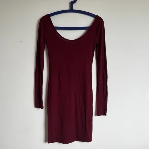 Vinröd långärmad tight klänning - Vinröd klänning med lång ärm och djup rundad urringning både fram och bak. Tight passform och kort längd, perfekt för dig som gillar en enkel men stilren look. Materialet känns mjukt och stretchigt.
