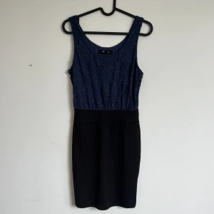 Blå spetsklänning med svart kjol - Snygg klänning från Forever 21 med blått spetsliv och svart kjoldel. Ärmlös modell med rund halsringning och figurnära passform. Perfekt för dig som vill ha en stilren och elegant look.