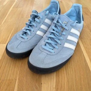 Adidas Gazelle i ljusblå mocka - Säljer ett par Adidas Gazelle i ljusblå mocka med vita ränder och svart sula. Skorna har klassisk snörning och Adidas-logga på sidan och innersulan. Perfekta för dig som gillar retrostil och vill ha något unikt i garderoben.