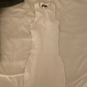 Vit ribbad kortklänning  - Säljer en vit ribbad kortklänning från New Yorker i storlek XS. Klänningen är ärmlös med rund halsringning och har en tight passform som framhäver figuren. Perfekt för varma dagar och enkel att styla med sneakers eller sandaler.
