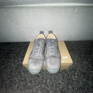 Grå mockasneakers från Christian Louboutin - Säljer ett par grå sneakers från Christian Louboutin i mocka med klassisk röd sula och snörning. Skorna har rund tå och diskreta sömdetaljer. Perfekta för dig som gillar exklusiva och stilrena sneakers. SKRIV I PM OM NI VILL KÖPA, kan även gå ner i pris