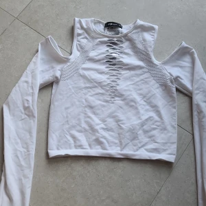 Vit långärmad topp med cut-out detaljer - vit långärmad topp med unika cut-out detaljer vid axlarna och ett snyggt snörningsmönster framtill. Toppen har en tight passform och är tillverkad i ett stretchigt material som sitter snyggt på kroppen.