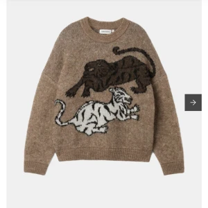 Stickad tröja med tiger-motiv från Carin Wester - Säljer en beige stickad tröja från Carin Wester med två stora tigrar i svart och vitt framtill. Tröjan är i ullmix och har en avslappnad passform med långa ärmar och rund hals. Perfekt för dig som gillar unika motiv!