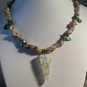 Halsband med pärlor och grönskimrande snäckdelar - Handgjort  unikt  halsband med oregelbundna pärlor i beige och grönt, dekorerat med guldfärgade detaljer. Hängsmycke i frostat glas insvept i guldfärgad tråd. Perfekt statement-piece för dig som gillar naturinspirerade smycken.