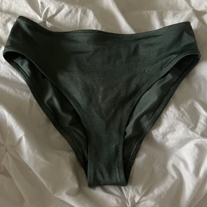 Mörkgrön bikini  - Säljer ett par mörkgröna bikinitrosor från H&M i klassisk modell. Trosorna har en hög midja och är tillverkade i ett mjukt och stretchigt material. 