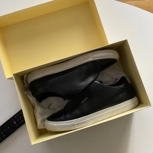  Axel Arigato skor - Säljer ett par stilrena svarta sneakers från Axel Arigato zip. Skorna är i skinn och har en klassisk rund tå. Perfekta för en clean och modern look. Storlek 43