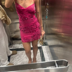 Peppermayo klänning  - Peppermayo klänning Supersnygg rosa kortklänning med tunna axelband och v-ringning. Klänningen är täckt av glittriga paljetter och har ett blommigt mönster som ger en extra wow-effekt. Perfekt för dig som vill sticka ut och glänsa! Sitter tight och framhäver figuren.