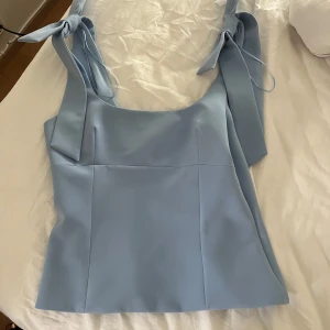 Ljusblå linnetopp med knytband Zara - Supersöt ljusblå linnetopp från Zara med breda axelband som knyts till stora rosetter. Toppen har en rak, figurnära passform och är tillverkad i ett slätt, lätt glansigt material.  Helt ny med prislapp kvar! Priset kan diskuteras 