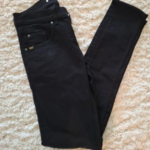 Svarta jeans från Tiger of Sweden - Svarta jeans från Tiger of Sweden med klassisk femficksdesign och diskreta detaljer. Jeansen har raka ben och normal passform, tillverkade i ett mjukt bomullsmaterial med lite stretch. Perfekta för en clean och stilren look.