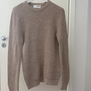Beige stickad tröja från Selected Homme - Snygg beige stickad tröja från Selected Homme i storlek S men passar även M. Tröjan har en grovstickad struktur, rund halsringning och ribbade muddar vid ärmslut och nederkant. Perfekt för lager-på-lager och enkel att matcha med jeans eller chinos. Skick 10/10 helt oanvänd tröja.