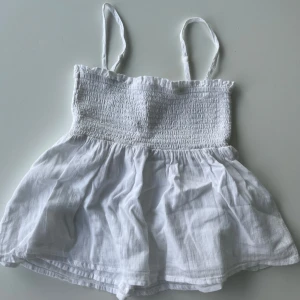 Vitt volanglinne - Supersöt vit linnetopp från Gina Tricot med smockad överdel och tunna axelband. Storlek 146/152 men passar XXS. Den är i fint skick använd fåtal gånger.