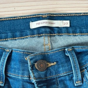 Levi's 710 Super Skinny jeans blå - Säljer ett par Levi's 710 Super Skinny jeans i klassisk blå tvätt. Modellen har smal passform hela vägen ner, normal midja och fem fickor. Jeansen är tillverkade i stretchigt denim för extra komfort och har snygga slitningar framtill.