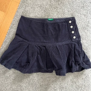 Manchesterkjol - Supersöt mörkblå lågmidjad kjol i manchester tyg med stor volang längst ned, silvriga knappar framtill på sidan. Säljer på grund av försliten, skulle säga storlek XS. Skriv vid frågor och mått! 🤗💗