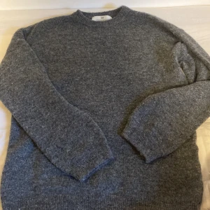 Grå stickad tröja från H&M - Mysig grå stickad tröja från H&M i storlek 146/152. Tröjan har rund halsringning, långa ärmar och är perfekt för kyliga dagar. Den har en klassisk, enkel design som funkar till många olika stilar.