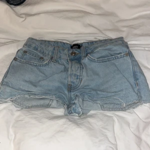Ljusblå lågmidjade jeansshorts  - Snygga ljusblå jeansshorts från 157 med råa, fransiga kanter och klassisk femficksmodell. Shortsen har bälteshällor, knapp och dragkedja framtill samt en skinnpatch med logga bak. Perfekta för sommardagar och festivalhäng.