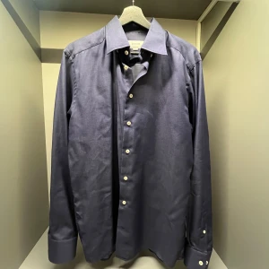 Mörkblå skjorta från Eton, slim fit - Snygg mörkblå skjorta från Eton i slim fit-modell. Skjortan har klassisk krage, vita knappar och långa ärmar med breda manschetter. Perfekt för dig som gillar stilrena och tidlösa plagg. Materialet är bomull som känns skönt mot huden.