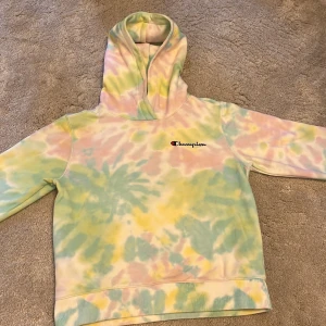 Pastellfärgad hoodie från Champion - Säljer en superfin hoodie från Champion i storlek Large. Tröjan har ett färgglatt tie-dye mönster i pastellfärger som gul, grön, rosa och blå. Klassisk huva och långärmad modell, perfekt för dig som gillar en chill och färgstark stil.