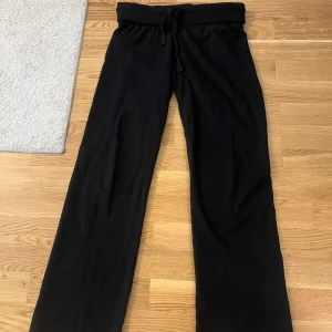 Populära Svarta mjukisbyxor från Nelly!! - Svarta mjukisbyxor från Nelly med normal passform och raka ben. Byxorna har resår och snörning i midjan för extra komfort. Perfekta för chill dagar eller när du vill vara bekväm men ändå se snygg ut.