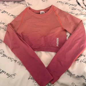 Rosa croppad tröja från Gymshark - Croppad långärmad tröja från Gymshark i två nyanser av rosa. Tröjan har en snygg ombre-effekt, ribbad nederkant och diskret snörning bak. Perfekt för träning eller chill dagar.