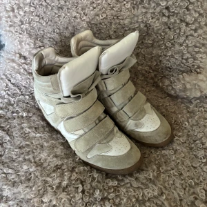 Beige wedge sneakers med kardborre - Snygga beige sneakers med inbyggd kilklack och flera breda kardborreband. Ovandel i mocka och skinn, detaljer i vitt och beige. Rund tå och platt yttersula i gummi. Perfekta för dig som vill ha en sportig look med extra höjd. Liknar Isabel Marant! Har tecken på använding.❤️