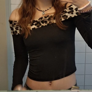 Svart offshoulder topp med leopardmönster - Säljer en snygg svart croppad offshoulder topp med lång ärm och bred leopardmönstrad kant upptill. Passar mig som brukar ha XS i toppar men jag säljer för har för breda axlar, därav använd endast ett fåtal gånger. 