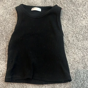 Svart ribbad linnetopp från Happiness - En svart ribbad linnetopp från Happiness, perfekt för dig som gillar en enkel och stilren look. Toppen är ärmlös med rund halsringning och har en tight passform. Materialet är stretchigt och bekvämt, vilket gör den lätt att matcha med allt.