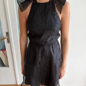 Svart kortklänning med halterneck helt ny - Supersnygg svart kortklänning från Bikbok med stor transparent rosett i nacken och öppen rygg. Klänningen har halterneck, markerad midja och är gjord i ett tunt, lätt material som ger en luftig känsla. Perfekt för dig som vill sticka ut med en elegant och trendig look. Helt ny med prislapp kvar!!
