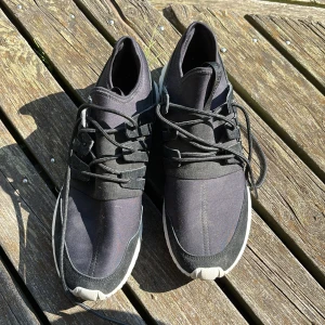 Svarta Adidas Tubular Shadow sneakers - Snygga svarta Adidas Tubular Shadow sneakers med modern design och chunky vit sula. Ovandelen är i textil och mocka med coola snörningsdetaljer. Perfekta för dig som gillar streetstyle och vill ha bekväma skor med unik look.