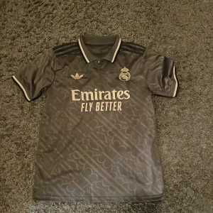 Real Madrid x Adidas grå fotbollströja S - Svart Real Madrid jersey från aidas tröjan är helt oanvänd och jag säljer pga att den är för stor, jävligt fet tröja till er skönt pris. Kom dm för mer info!