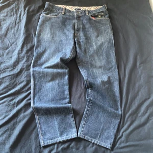 Mörkblå jeansbyxor från Burberry - Snygga mörkblå jeans från Burberry med klassiskt rutigt foder i midjan och bakficka med knapp. Rak passform och diskreta detaljer som ger en stilren look. Perfekta för dig som gillar premiumkänsla och tidlös design.