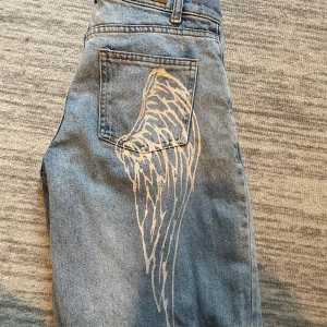 Lågmidjade y2k jeans - Säljer ett par blå jeans från subdued med ett coolt vingeprint på bakfickan. Klassisk femficksmodell i denim med normal passform och raka ben. Lågmidja.
