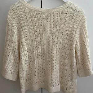 Stickad cremevit tröja med hålmönster - Superfin cremevit stickad tröja. Hål stickad fram till och stängd i bak. Trekvarts ärm. Helt ny utan pris lapp