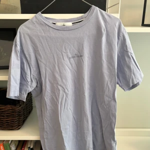 Ljusblå Stone Island t-shirt - Snygg ljusblå t-shirt från Stone Island med diskret logga tryckt på bröstet. Klassisk passform med rund hals och korta ärmar. Perfekt basic-plagg i mjuk bomull som funkar till allt.