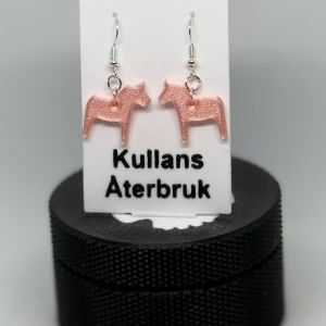 Dalahästörhängen önska färg sommar - Unika Dalahäst-örhängen – Perfekt för alla som älskar svensk design!  Dessa charmiga örhängen i form av dalahästar – ett stilfullt och hållbart val! De vackra  färgerna ger en modern twist på en älskad svensk klassiker.   ✨ Lätta och bekväma att bära ✨ Nickelfria krokar för känsliga öron ✨ Perfekt som present eller för att lyfta din egen stil  Gör ett statement med dessa unika smycken från Kullans Återbruk – svensk tradition möter hållbarhet! Önska färg. 
