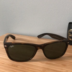 Ray-Ban Wayfarer brunmelerade solglasögon - Klassiska Ray-Ban Wayfarer solglasögon med brunmelerad båge och mörka glas. Snygg fyrkantig form och diskret logga på sidan. Kommer med original svart fodral och putsduk. Perfekta för dig som vill ha en tidlös och cool look.