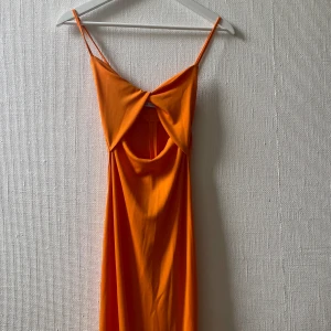Orange klänning från Zara - Snygg orange knälång klänning från Zara med tunna axelband och cool cut out-detalj framtill. Klänningen har en figurnära passform och är tillverkad i ett mjukt, slätt material. Använd bara 2-3 gånger.