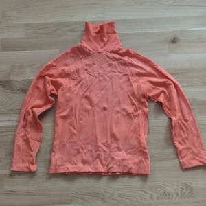 Vintage 60tal Korallfärgad polotröja i bomull - Säljer en korallfärgad polotröja med lång ärm och ribbad hög krage. Typisk 60tals tröja i polyester skulle jag tro. Det finns en liten lapp där det står stl 160 men den passar till xxs/xs. Den är lite repad på ena ärmen, se bild.